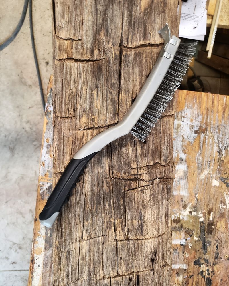 A wire brush used to clean barnwod sitting on top of a hand hewn beam